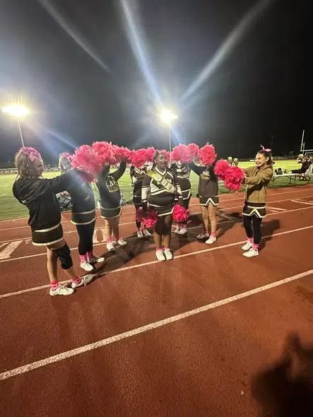 Bears cheerleaders raising their poms together on the field under the lights